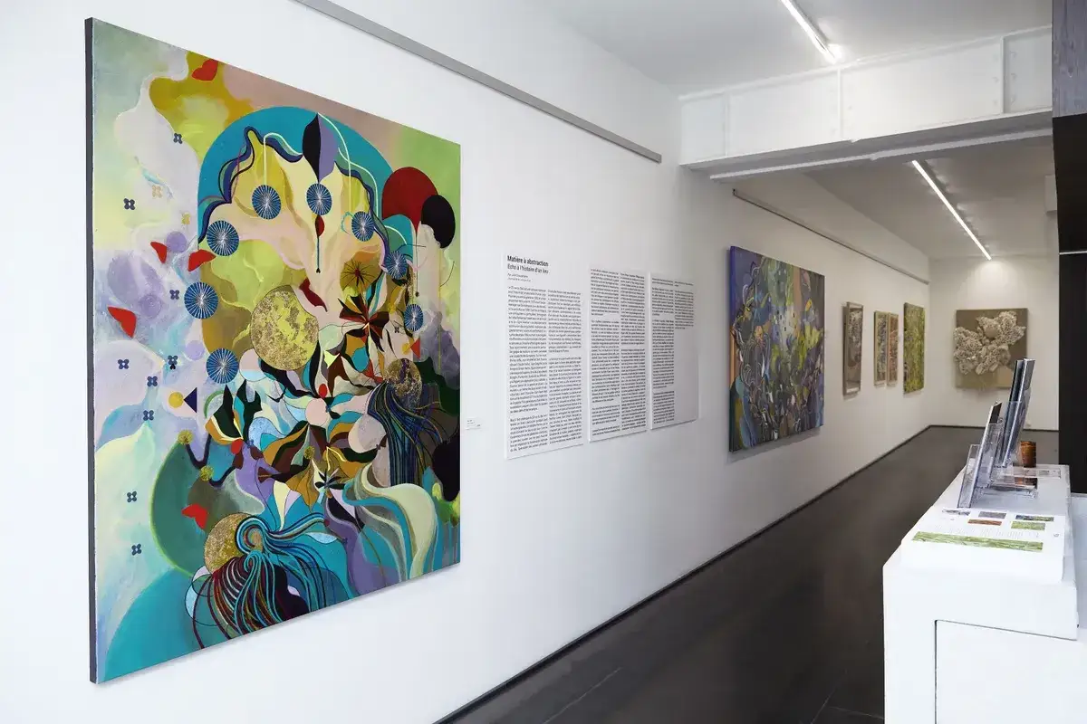 Découvrez comment fonctionne une galerie d'art : une œuvre abstraite colorée, des textes explicatifs et d'autres toiles dans un espace lumineux.