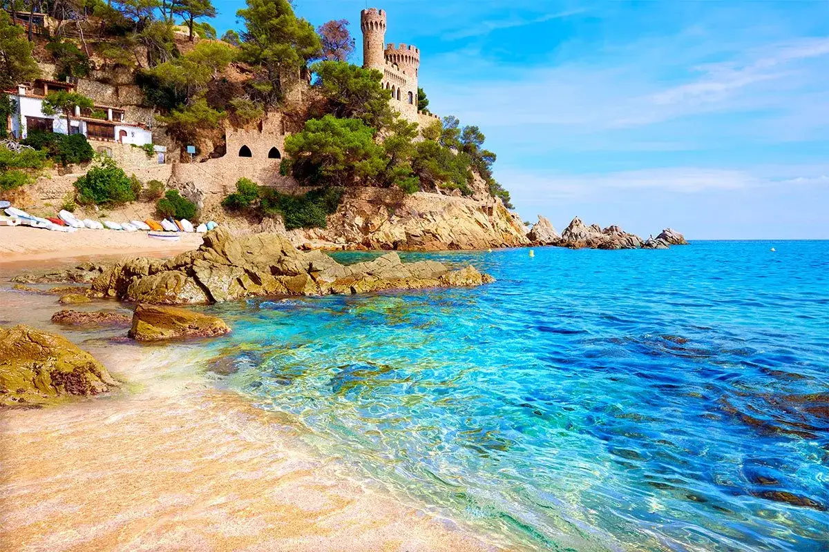 Zamek na klifie nad turkusowym morzem w Tossa de Mar. Piękna plaża z łodziami i skalistym wybrzeżem.