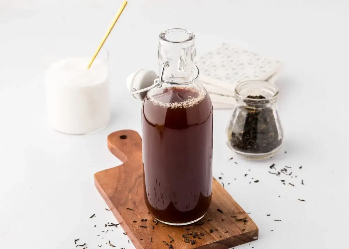 Zutaten für eistee sirup selber machen: eine Flasche dunkler Eistee, ein Glas Zucker und ein Glas lose Teeblätter.