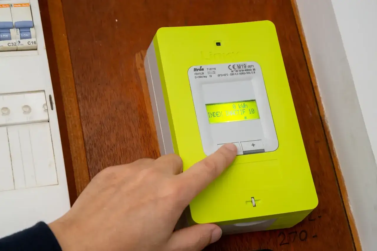 Main verte, compteur Linky. Un doigt appuie sur un bouton. Attention au vol d'électricité, code pénal.