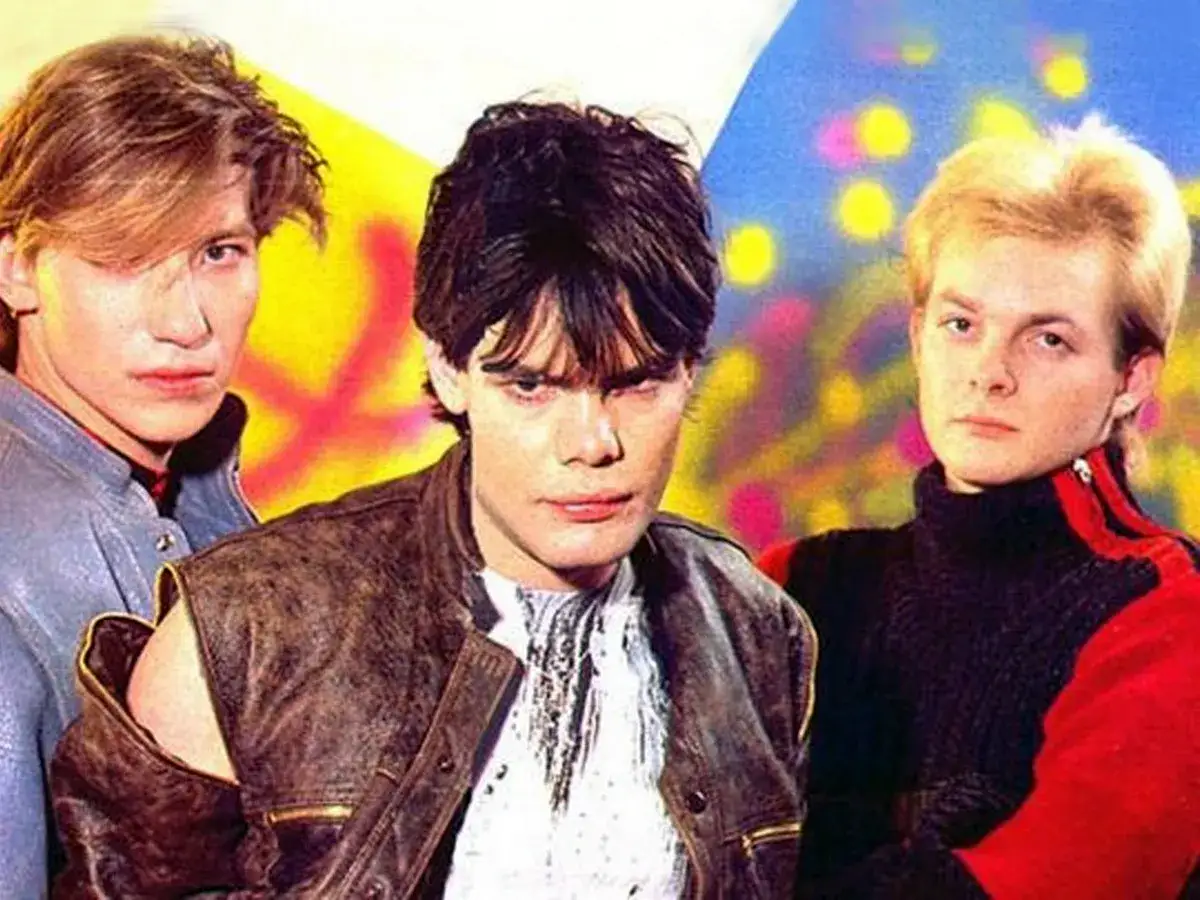 Trois jeunes hommes, un groupe allemand des années 80, posent devant un fond coloré.