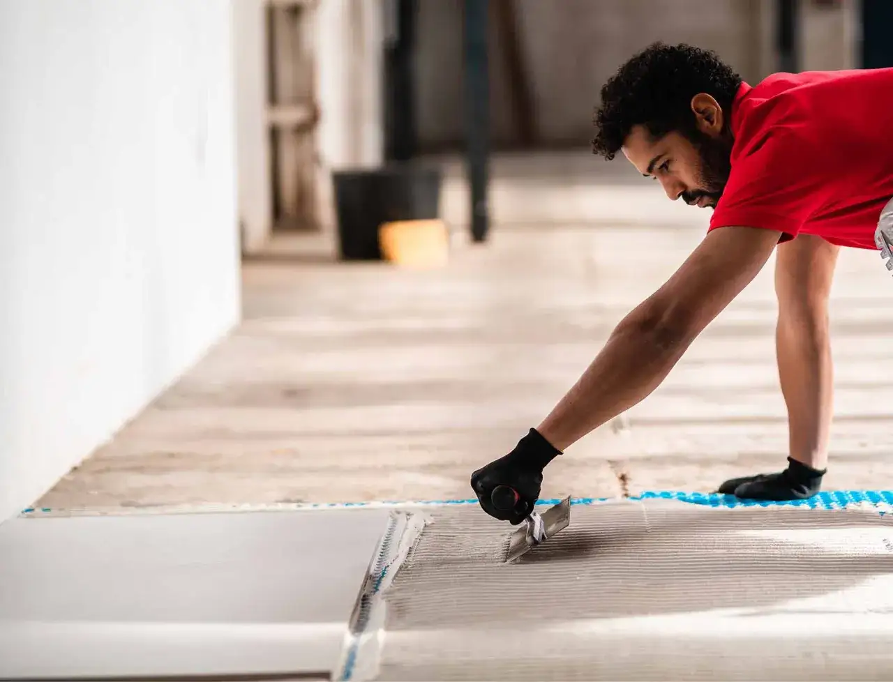 A tiler applies adhesive to the floor, preparing to lay tiles. He's focused on the task, whether it's porcelain vs ceramic tile.