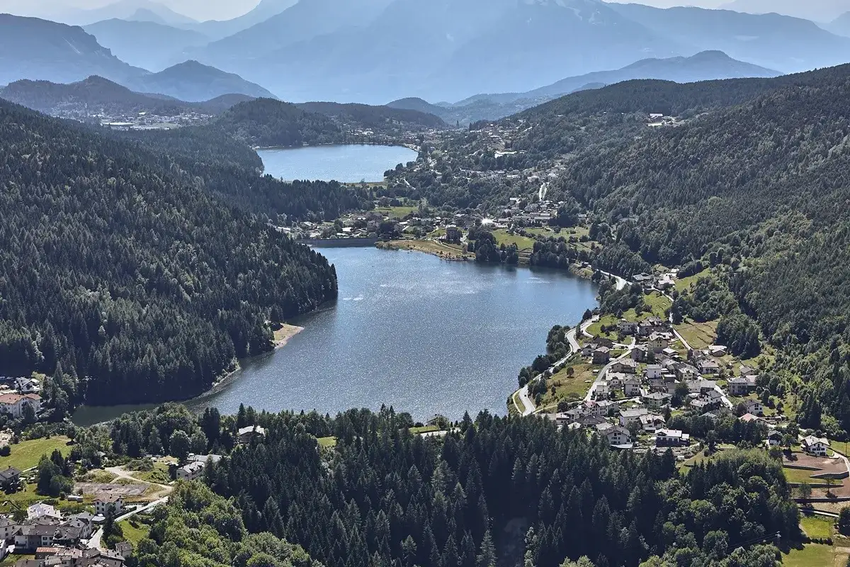 Panoramica della **montagnaga di Pinè** con due laghi scintillanti, circondati da fitti boschi e pittoreschi villaggi.