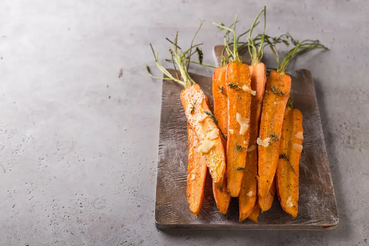 Carottes rôties, tendres et caramélisées, parsemées de copeaux de parmesan et de thym frais sur une planche en bois. Un délice simple et savoureux.