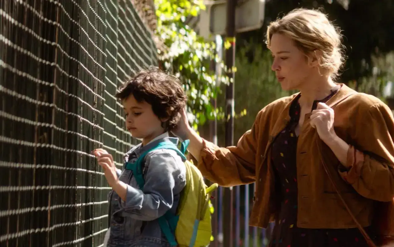 Una donna accarezza un bambino con uno zaino davanti a una recinzione. Le recensioni de 