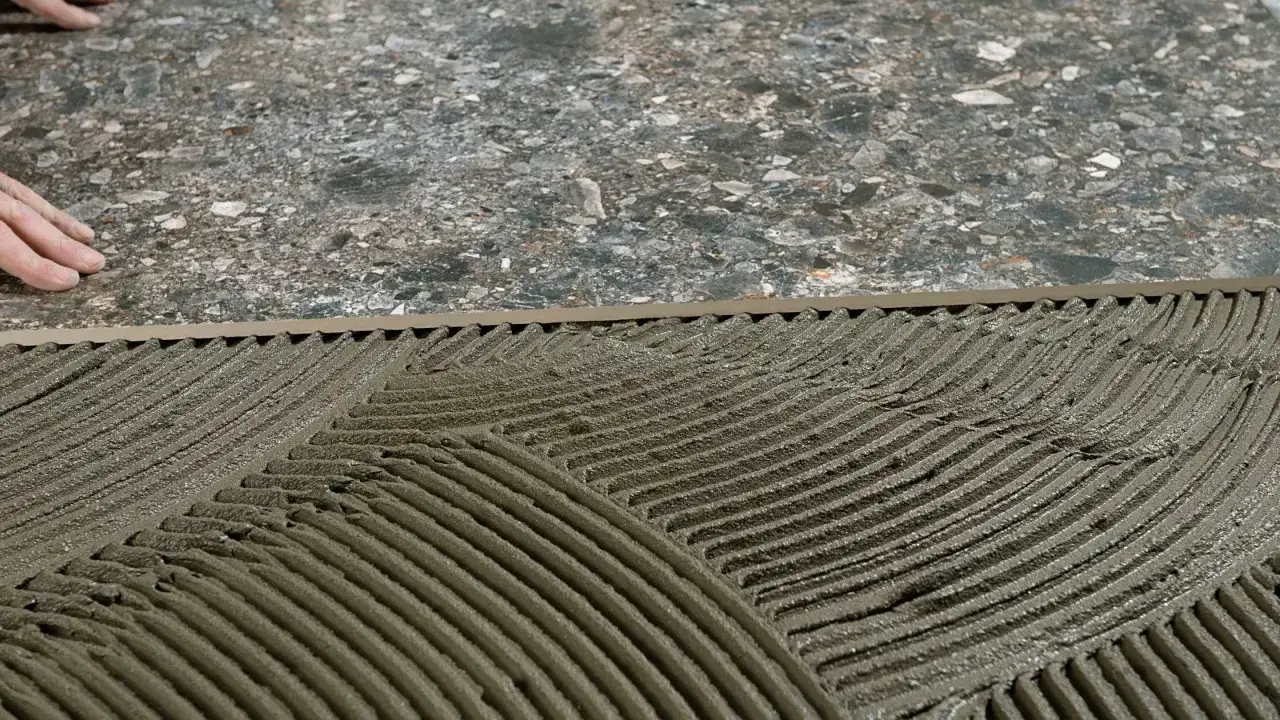 Pose de mortier pour carrelage collé. Mains ajustant une grande dalle sur le lit de colle fraîchement étalée.