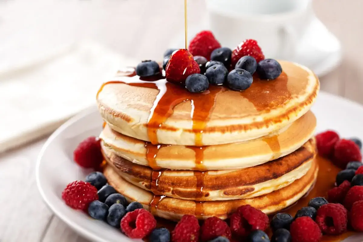 Pile de pancakes de farine compl&egrave;te, napp&eacute;s de sirop et garnis de framboises et myrtilles. Un d&eacute;lice pour le petit-d&eacute;jeuner.