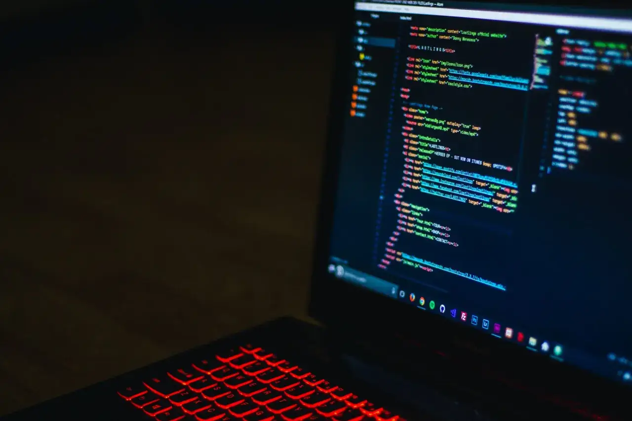 Laptop z podświetlaną na czerwono klawiaturą, na ekranie kod. Idealne narzędzie dla każdego testera oprogramowania.