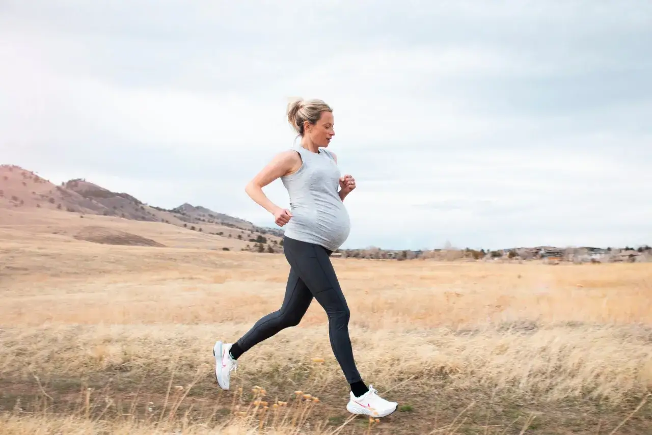Donna incinta corre in un paesaggio naturale, godendosi l'aria aperta e mantenendosi attiva durante la gravidanza.