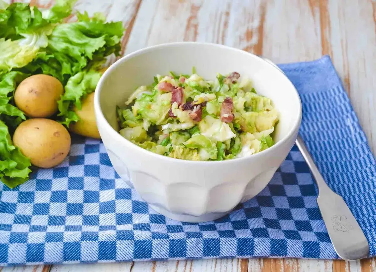Sch&uuml;ssel mit einem Salat aus gehackten Endivien untereinander, garniert mit Speck. Daneben liegen frische Kartoffeln und Salatbl&auml;tter.
