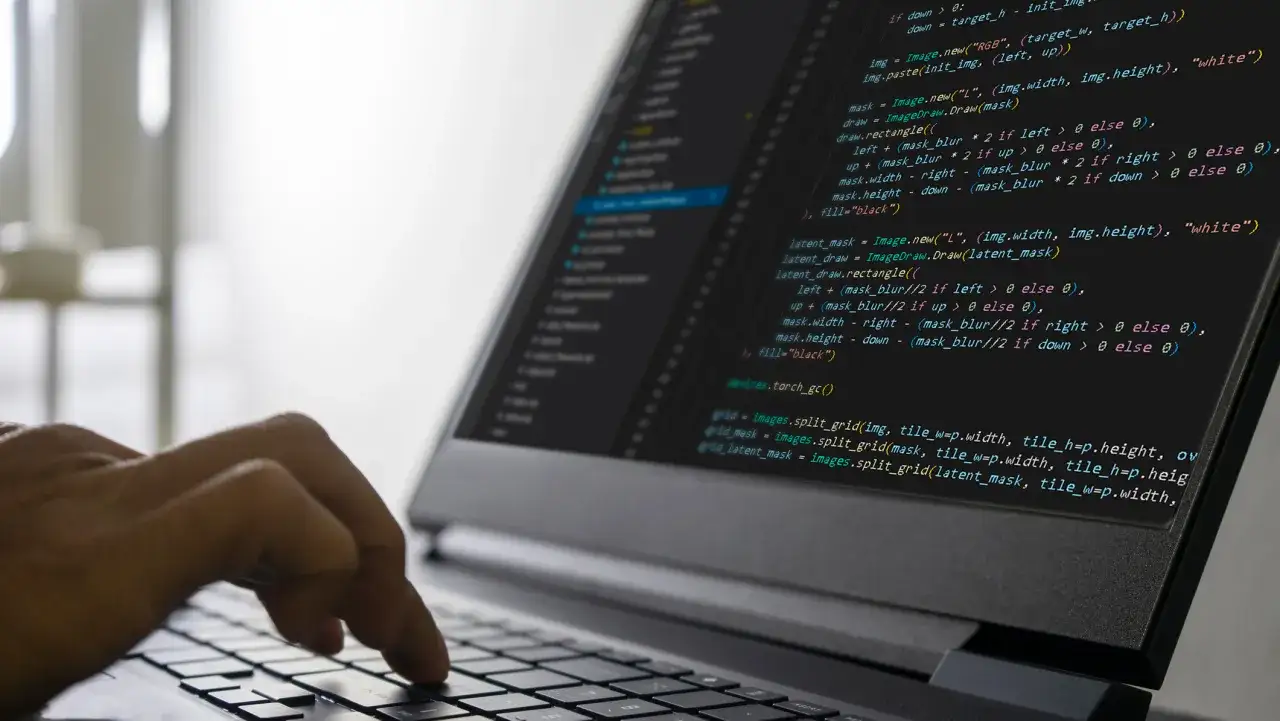 Ręka pisze kod na laptopie, pokazując ścieżkę, jak zostać programistą.