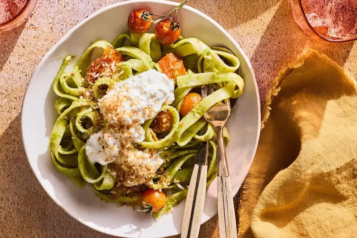 Grön pasta med krämig burrata, körsbärstomater och ströbröd. En härlig burrata pasta som ser utsökt ut.