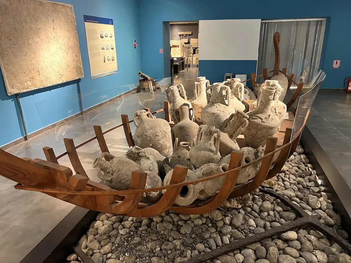Starożytne amfory i inne artefakty wypełniają drewniany kadłub statku, tworząc fascynującą ekspozycję muzealną.