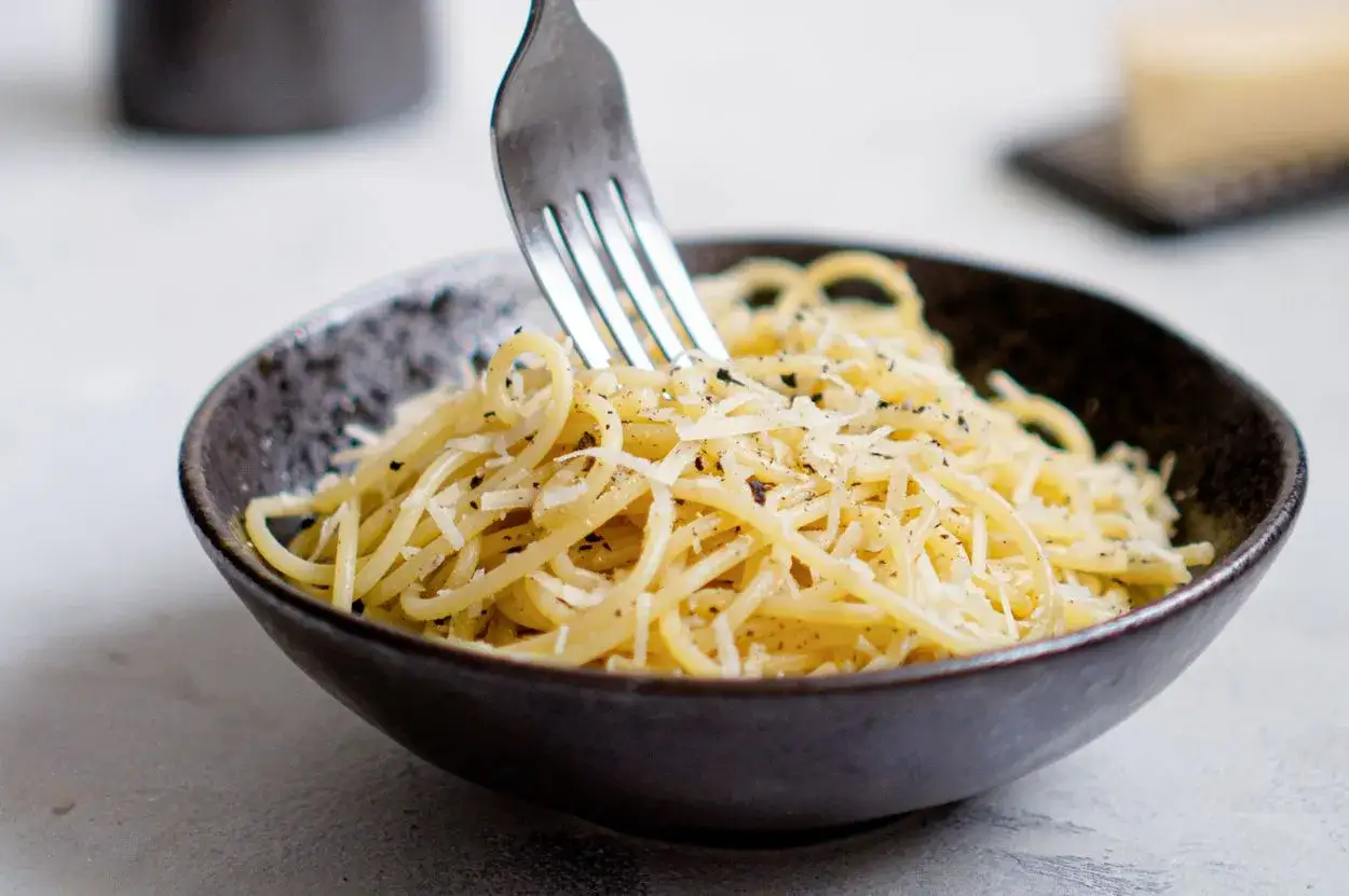 Widok z bliska na miskę pełną spaghetti posypanego parmezanem i pieprzem. Idealny przykład, jak zrobić spaghetti.