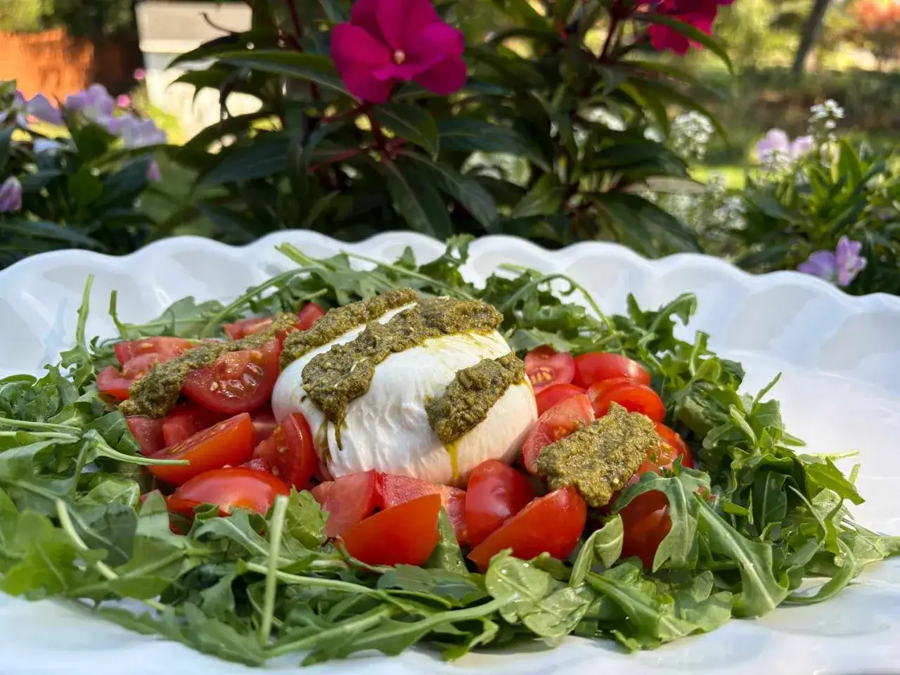 Burrata mit Rucola und Tomaten, betr&auml;ufelt mit Pesto. Ein frischer Genuss im Gr&uuml;nen.
