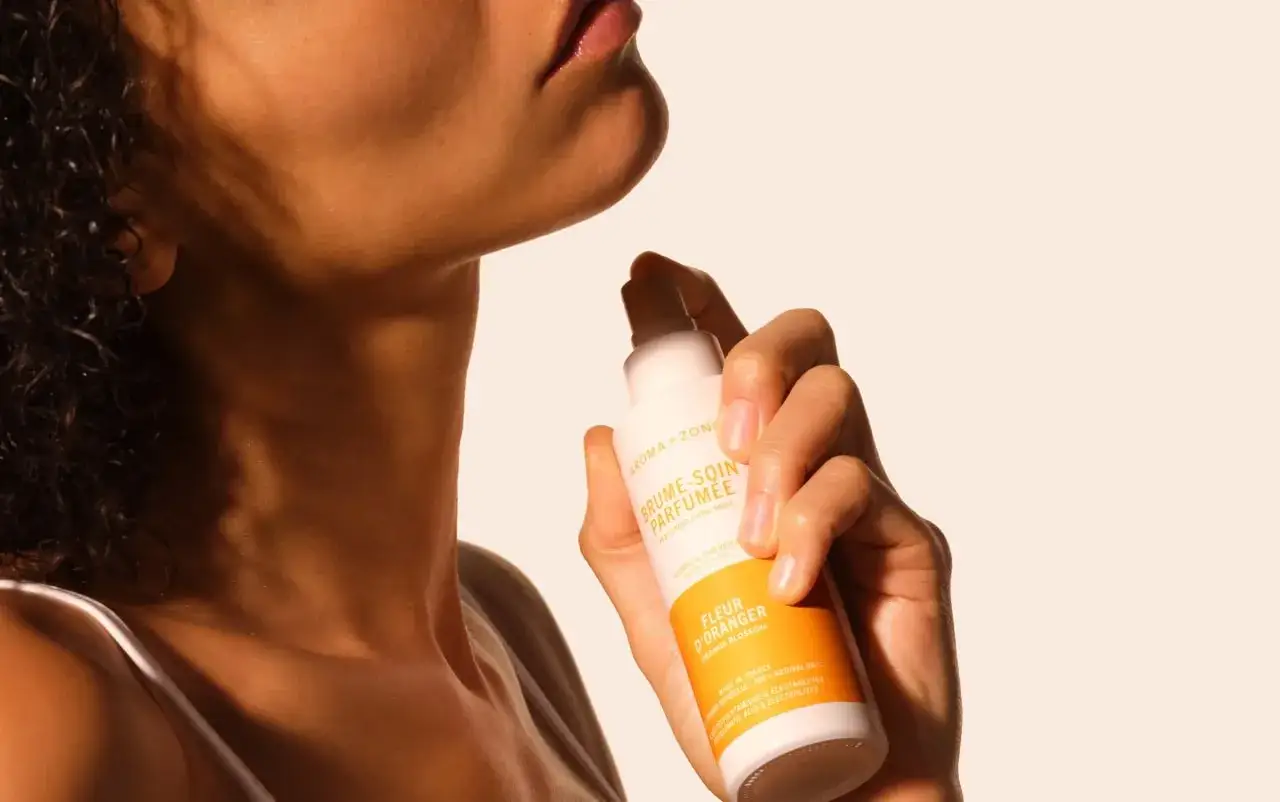 Une main vaporise une brume parfumée Fleur d'Oranger sur le cou. Apprenez comment utiliser une brume parfumée pour un sillage délicat.