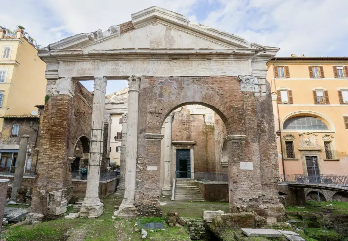 Antico portico di Ottavia a Roma, con rovine di colonne e mattoni antichi, sullo sfondo edifici moderni.