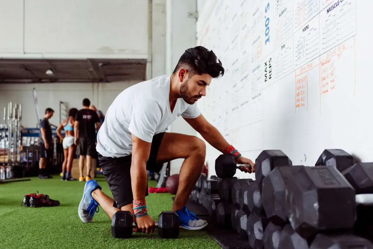Ein Mann holt Hanteln f&uuml;r sein Training. Die Wand zeigt Trainingspl&auml;ne, wie trainiert man effektiv.