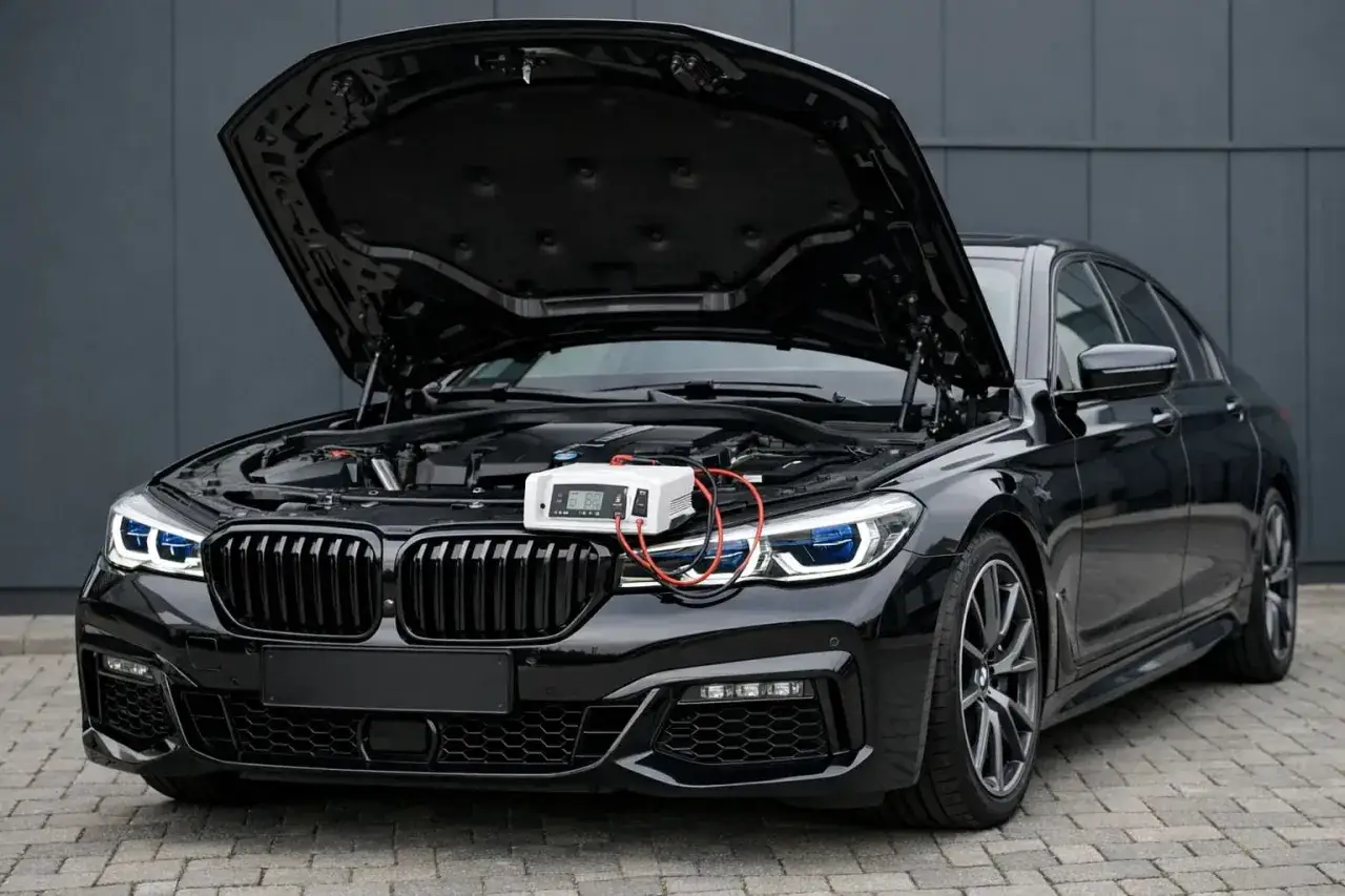 Czarny BMW 745Le z otwartą maską, podłączona ładowarka akumulatora.