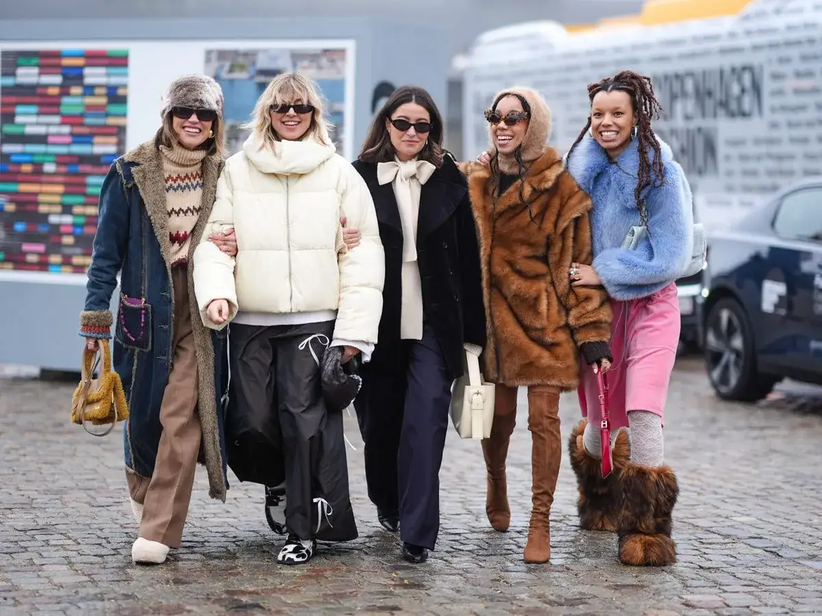 Cinq femmes stylées marchent ensemble, s'habiller chaudement avec des manteaux en fausse fourrure, des doudounes et des bottes hautes.