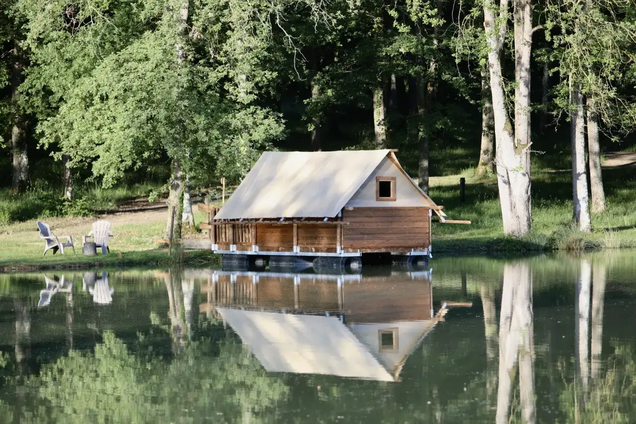 Un charmant whakka lodge en bois et toile flotte sur un lac paisible, entouré d'arbres verdoyants.