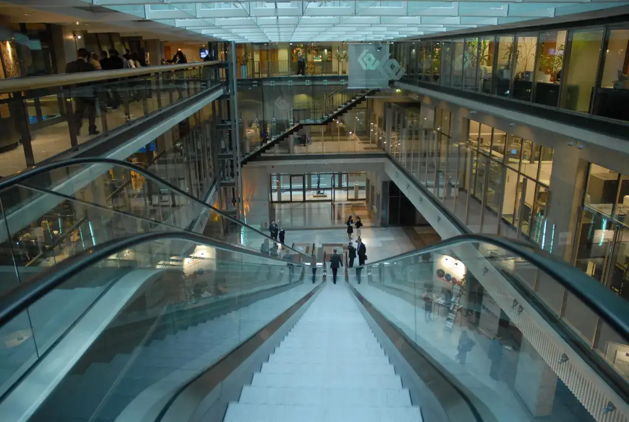 Nowoczesne atrium, ruchome schody i ludzie w garniturach. W tle biura, gdzie zapadają decyzje dotyczące akcji polskich sp&oacute;łek.