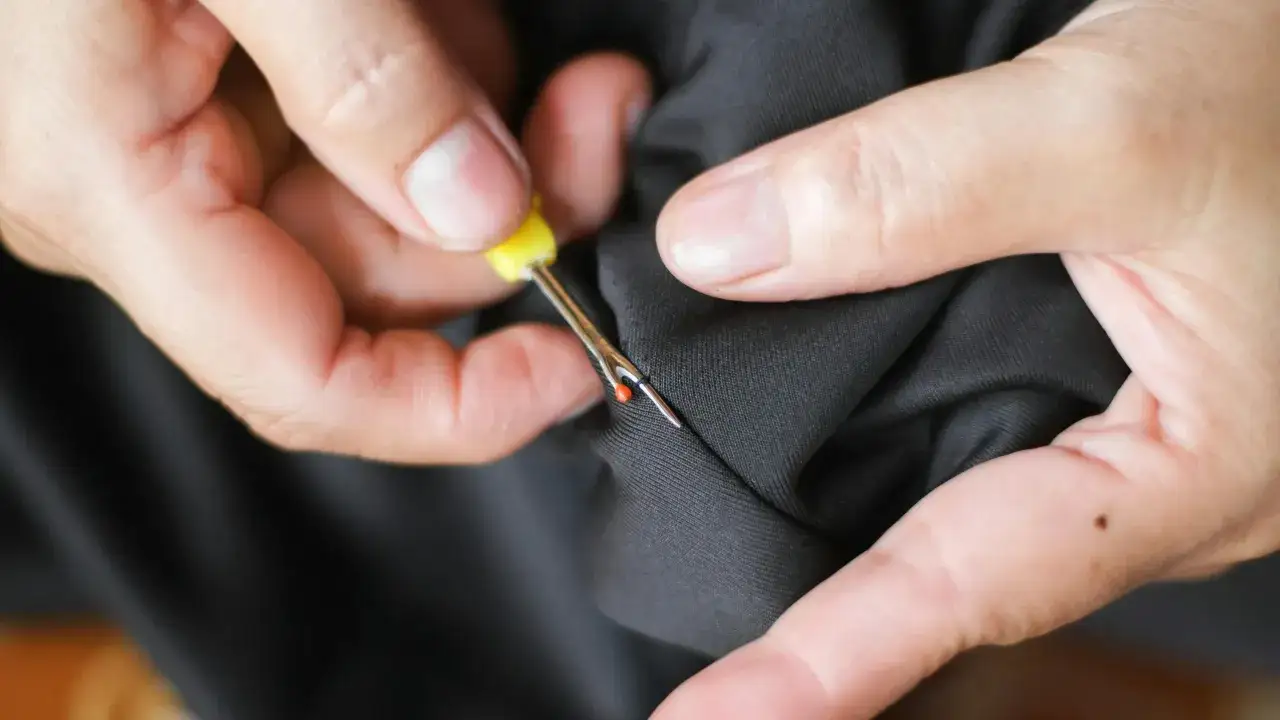 Hands use a seam ripper to open a pocket on black fabric. This is how suit pockets are sewn shut to maintain their shape during shipping.