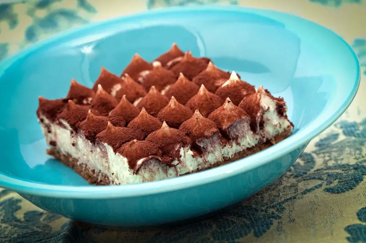 Un délicieux tiramisu, prêt à être dégusté, dans un plat bleu vif. Une invitation à suivre la recette !