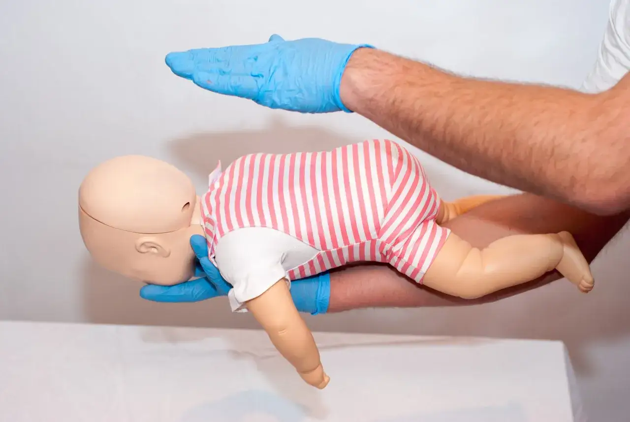 Esercitazione sulla manovra di Heimlich per bambini: mani guantate sorreggono un manichino neonato, simulando un intervento salvavita.
