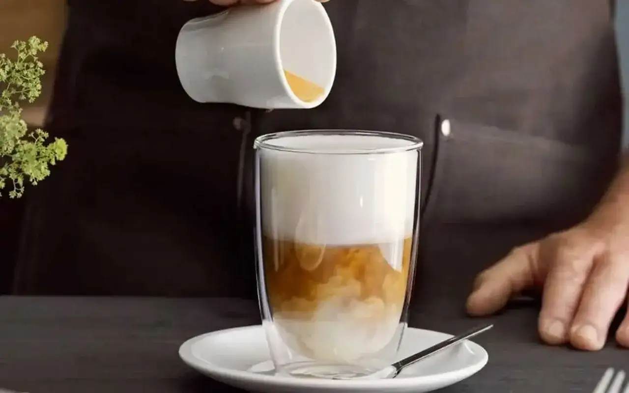 En barista häller upp en flat white i ett glas.