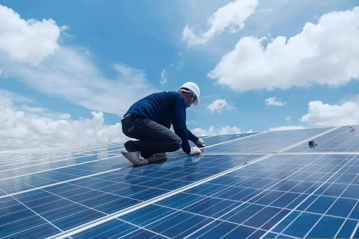 Instalator pracuje przy panelach fotowoltaika do 150 kw bez pozwolenia na budowę. Błękitne niebo z chmurami.