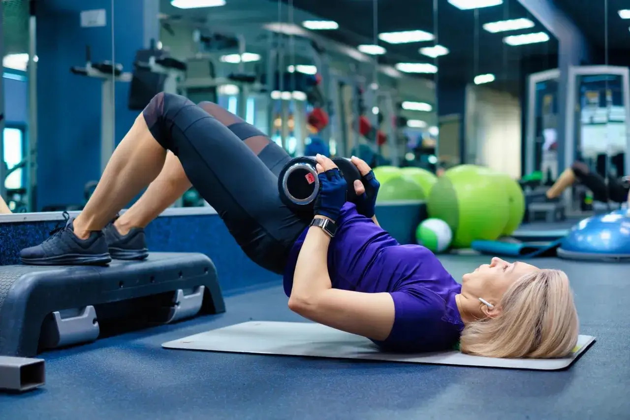 Mujer realiza ejercicio glúteo con pesa en gimnasio.