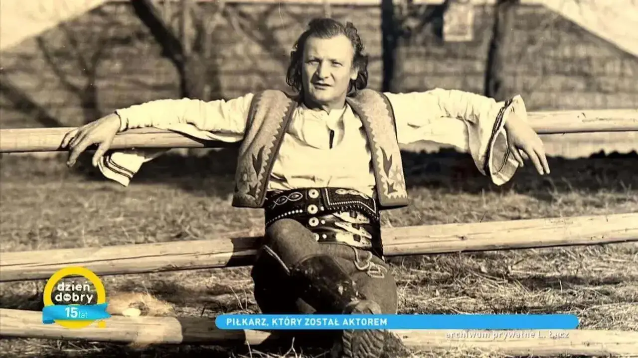 Marian Łącz, piłkarz i aktor, siedzi na płocie w stroju ludowym.