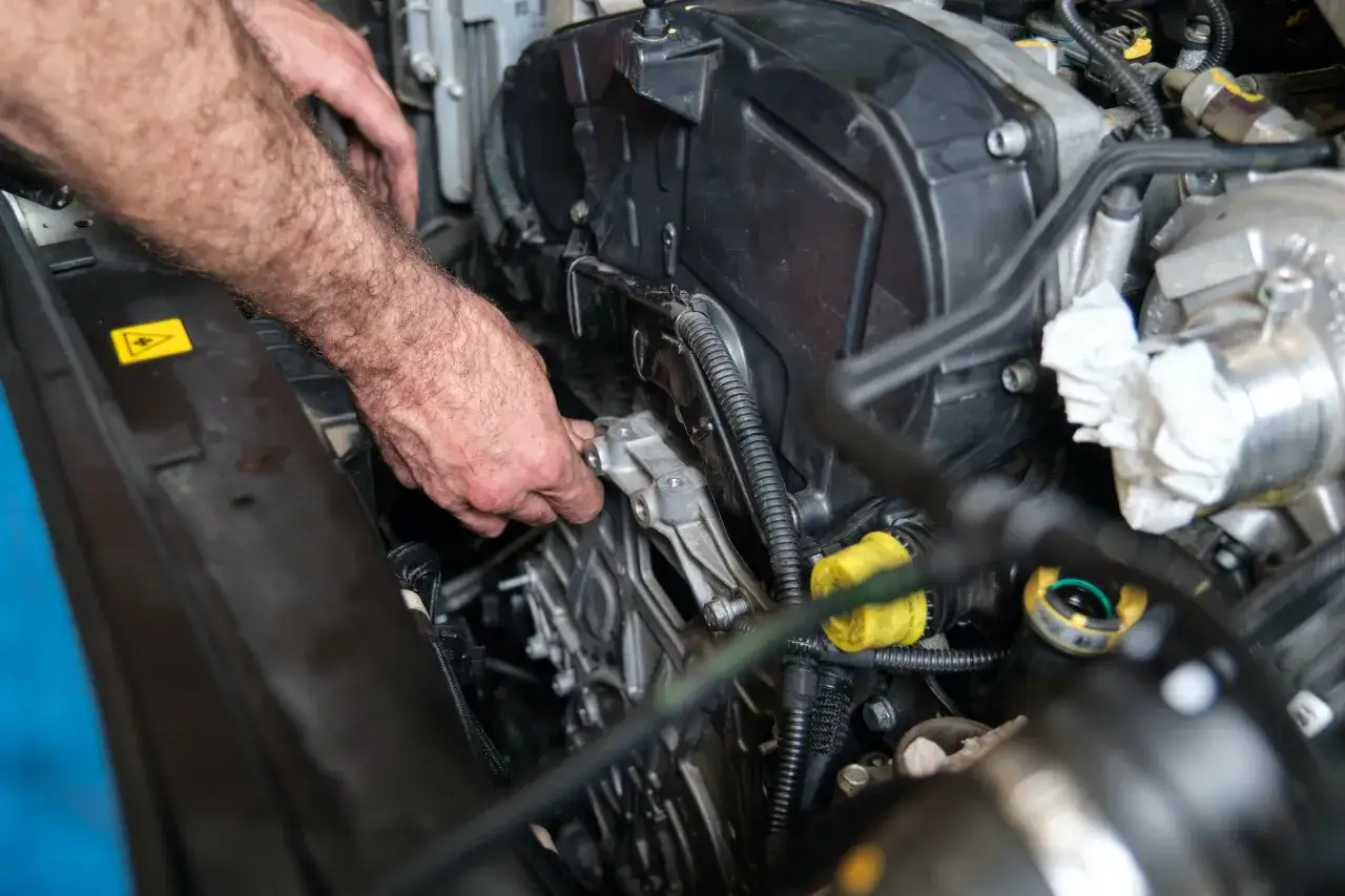Mec&aacute;nico trabajando en el motor de un coche, ajustando la correa de distribuci&oacute;n.