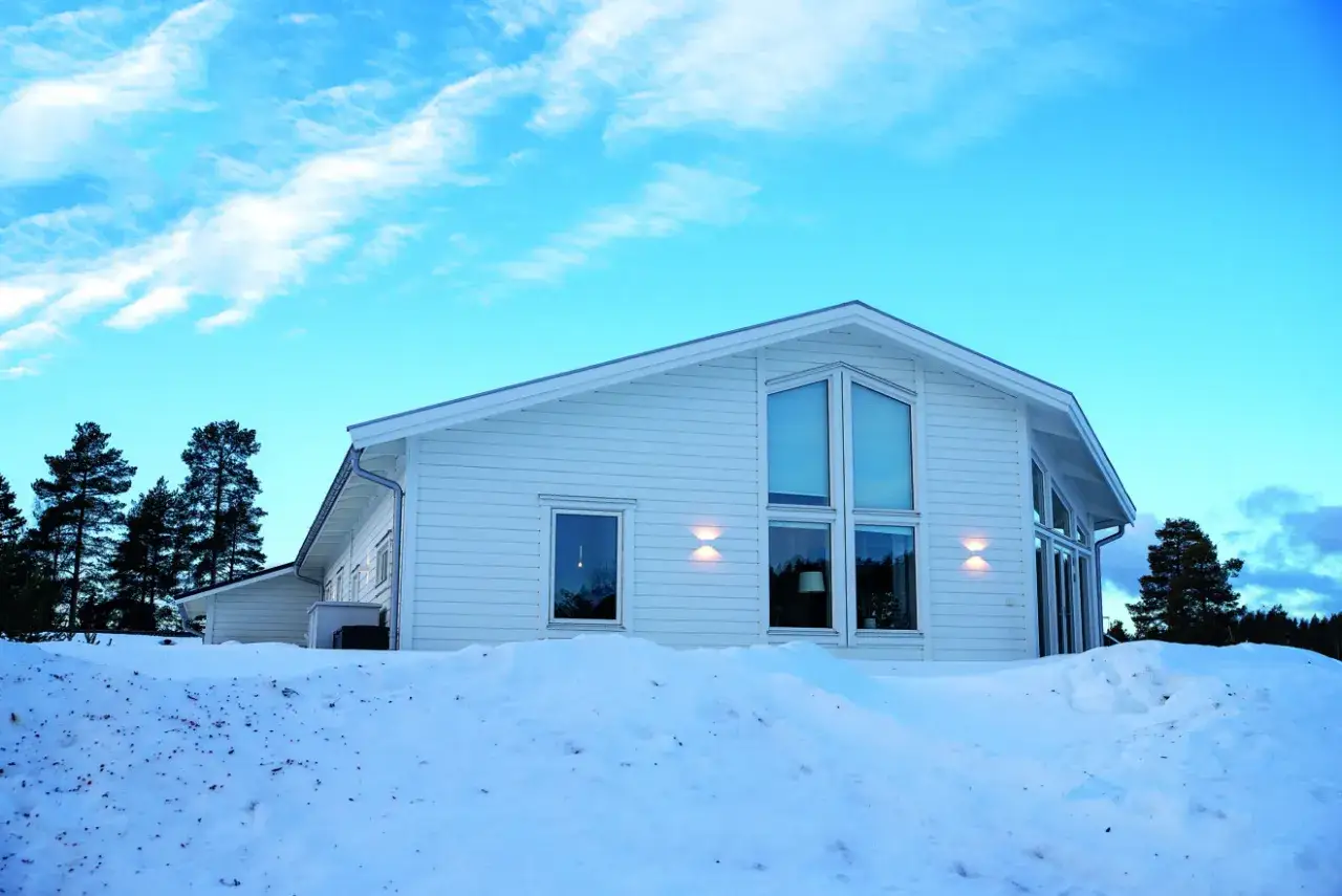 Vitt hus i snölandskap med stora fönster, perfekt för ett off grid-liv i Sverige.