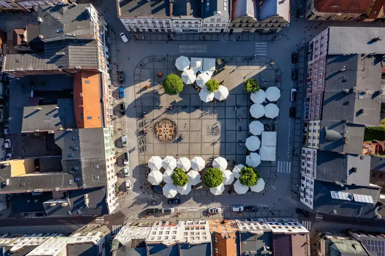 Widok z lotu ptaka na rynek w Kościerzynie, z białymi parasolami, drzewami i budynkami.