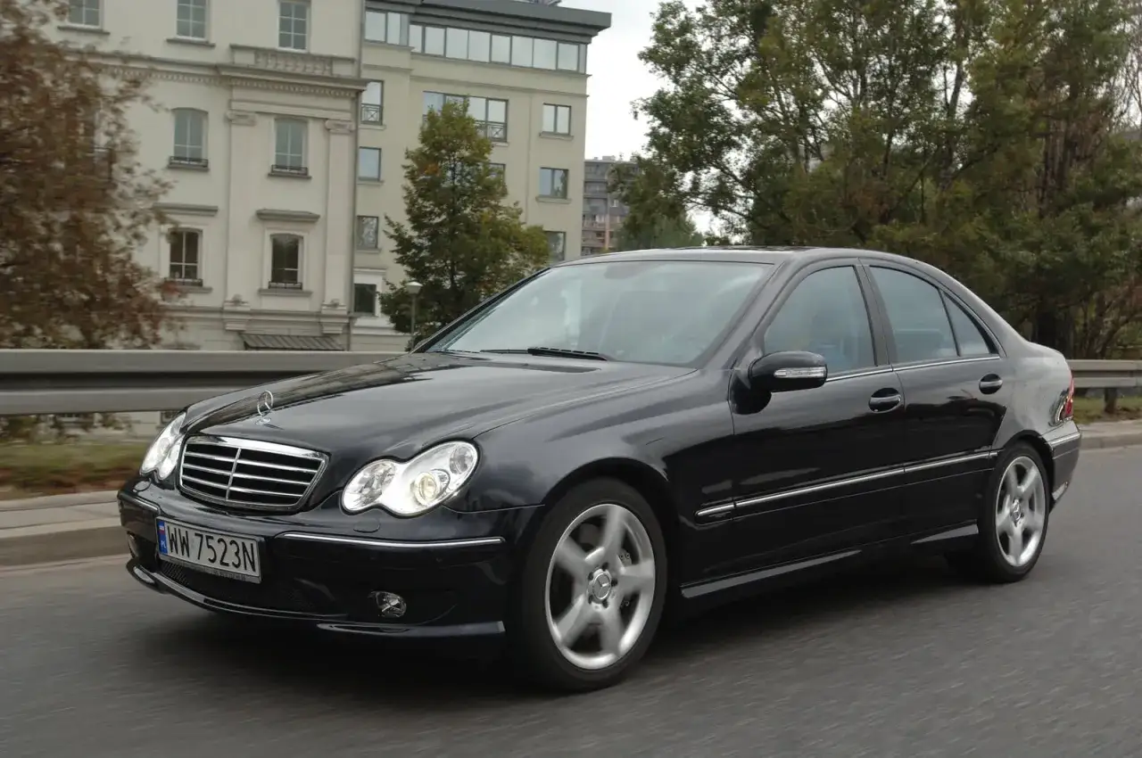 Czarny Mercedes W203 w ruchu, świeci się jedna żarówka mijania, sugerując potrzebę wymiany.