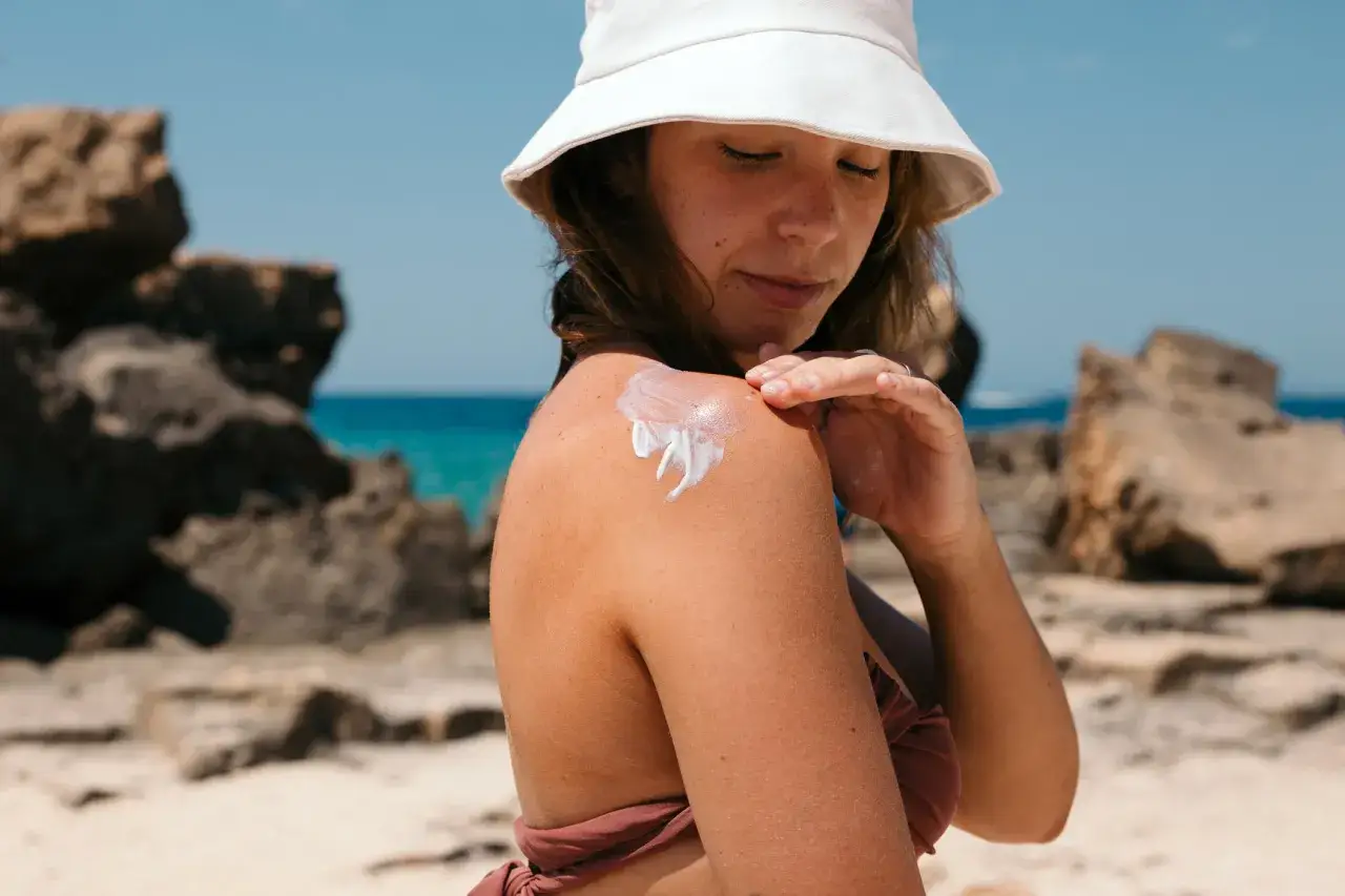 Donna applica crema solare sulla spalla, consapevole che l'olio abbronzante fa male. Sulla spiaggia, il sole splende.