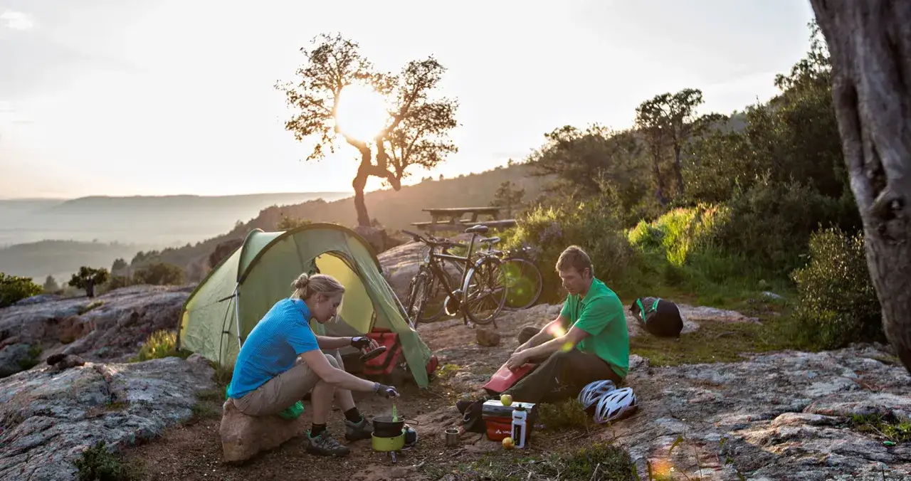 Ein Paar genie&szlig;t das **wildcampen Italien** bei Sonnenuntergang. Fahrr&auml;der stehen neben dem Zelt, w&auml;hrend sie kochen.