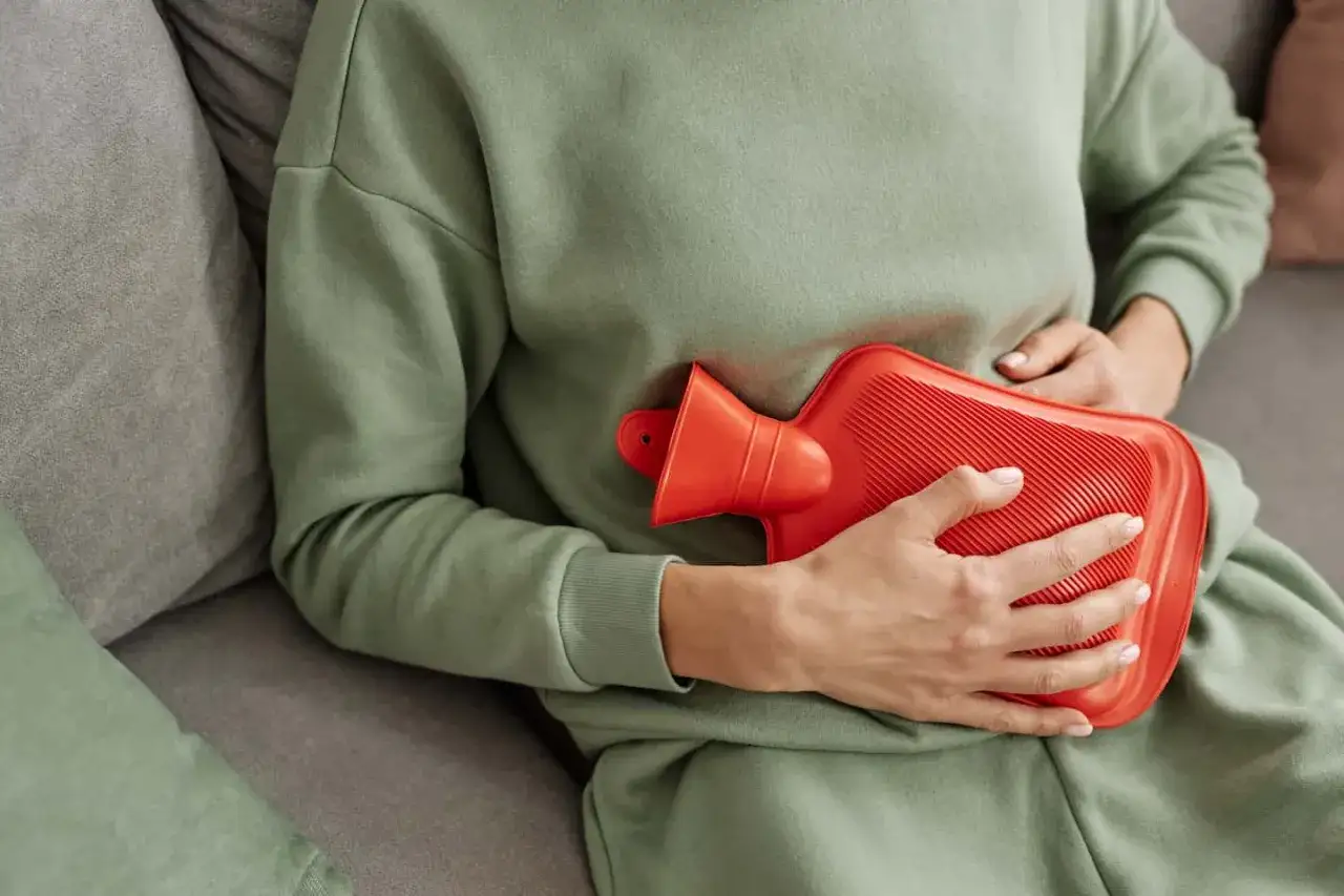 Eine Person hält eine Wärmflasche gegen den Bauch. Das hilft gegen Blähbauch und Bauchschmerzen.