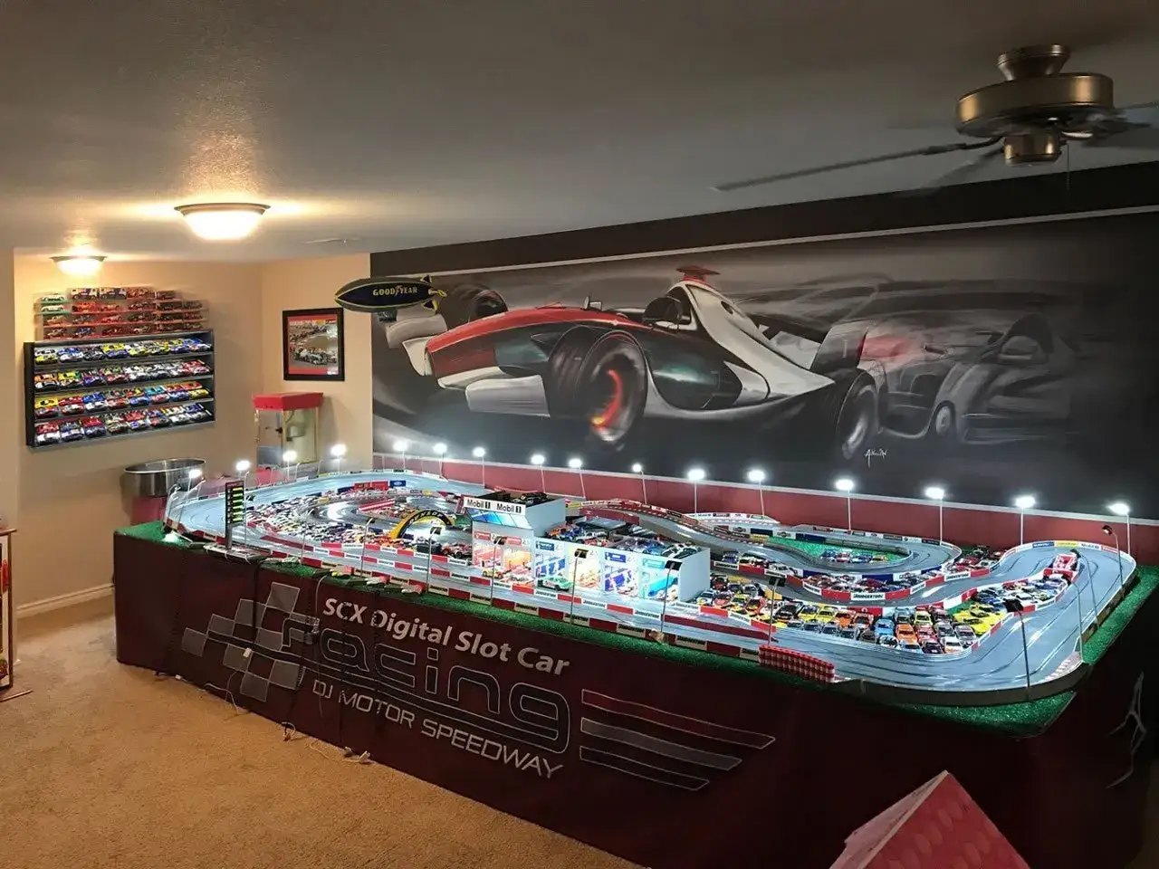 Scenografia di una pista per auto da corsa in miniatura, con una vasta collezione di modellini esposti su una parete. La **tabella scala modellismo auto** è dettagliata, con un circuito complesso e auto in gara.