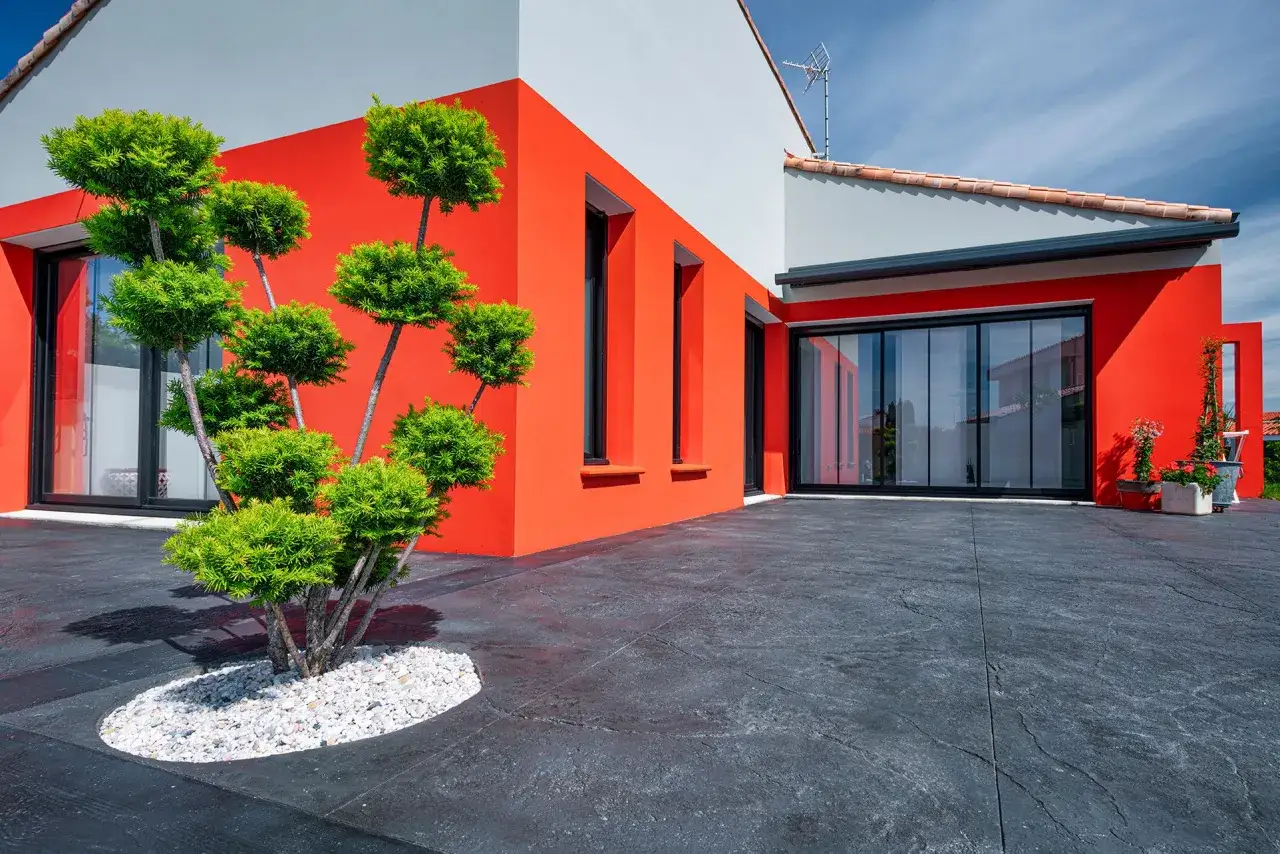 Une maison moderne aux murs orange vif et gris, avec une terrasse en béton texturé. Faut-il déclarer une terrasse en béton ?