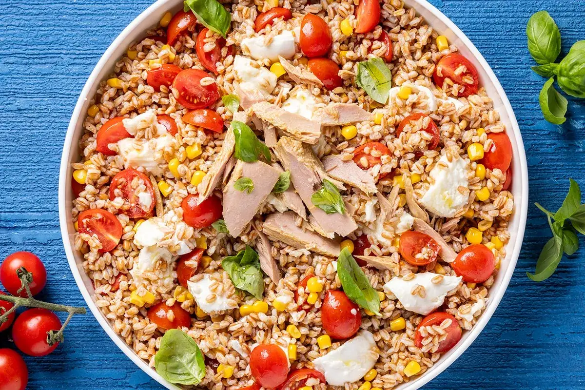 Un'insalata di farro estiva ricca di pomodorini, mais, mozzarella e tonno, guarnita con basilico fresco. Perfetta per un pasto leggero e gustoso.