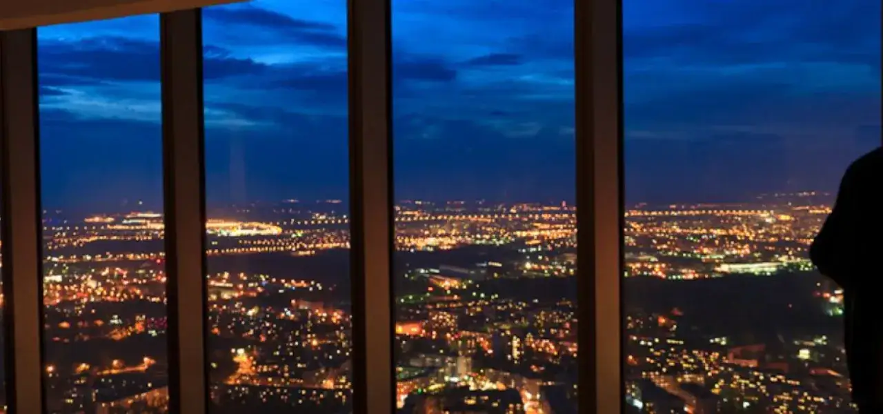 Widok z okna na nocne miasto, światła migoczą w oddali. Imponująca sky tower wysokość robi wrażenie.