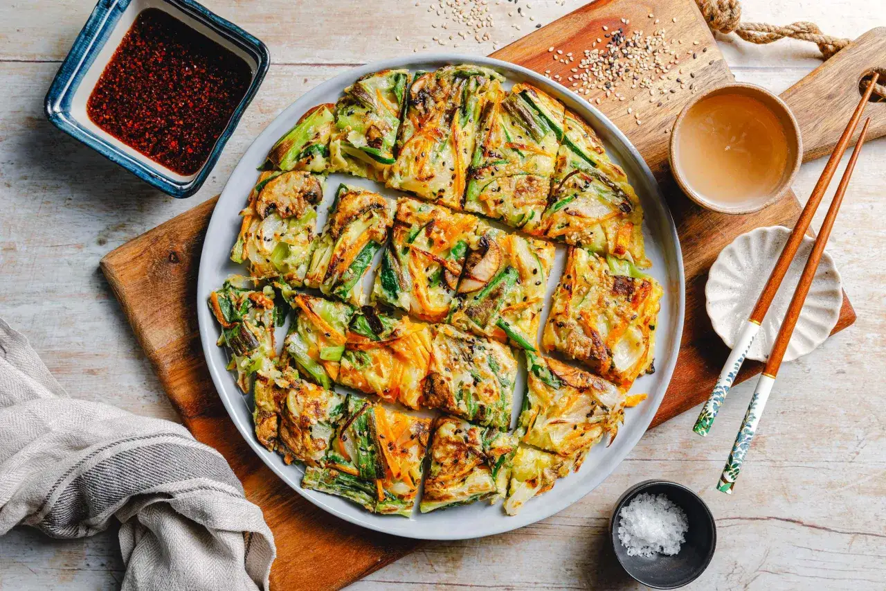 Herzhafte koreanische Pfannkuchen mit Gemüse, Pilzen und Sesam, serviert mit Dip und Stäbchen.