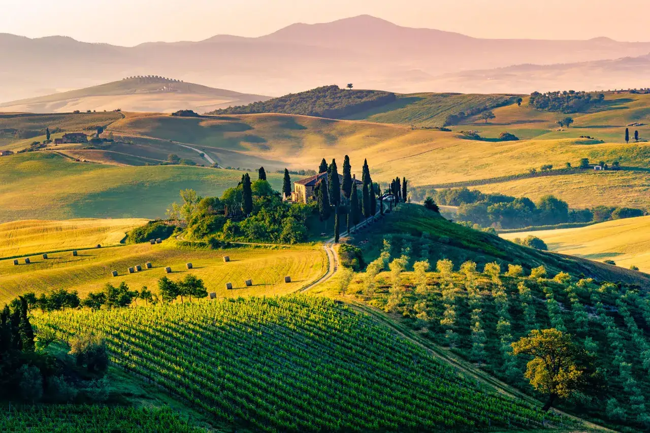 Colline ondulate del Val d'Orcia al tramonto, con una casa in cima a una collina circondata da cipressi e vigneti.