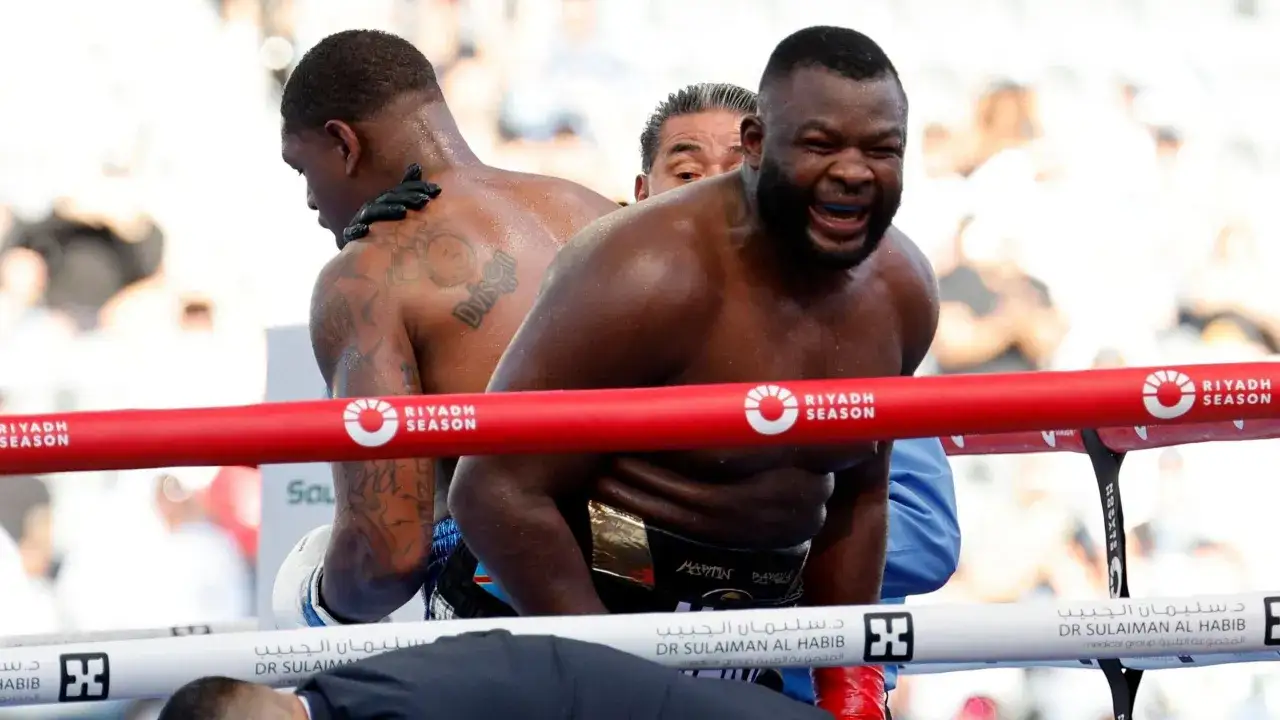 Martin Bakole, med bl&aring;tt tandskydd, uttrycker sm&auml;rta i ringen. En annan boxare syns i bakgrunden.