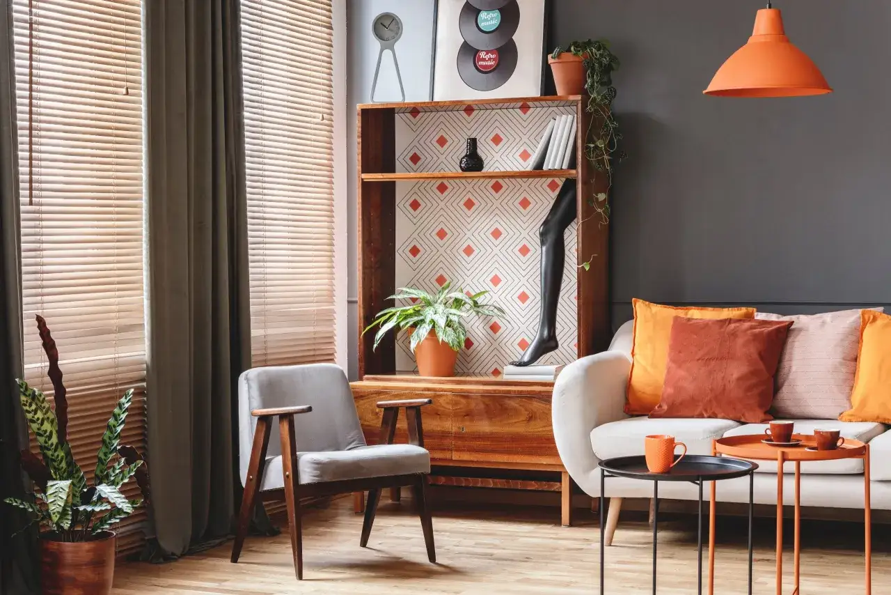 Un accogliente soggiorno con arredamento vintage casa: divano bianco, poltrona grigia, libreria in legno e tavolini arancioni.