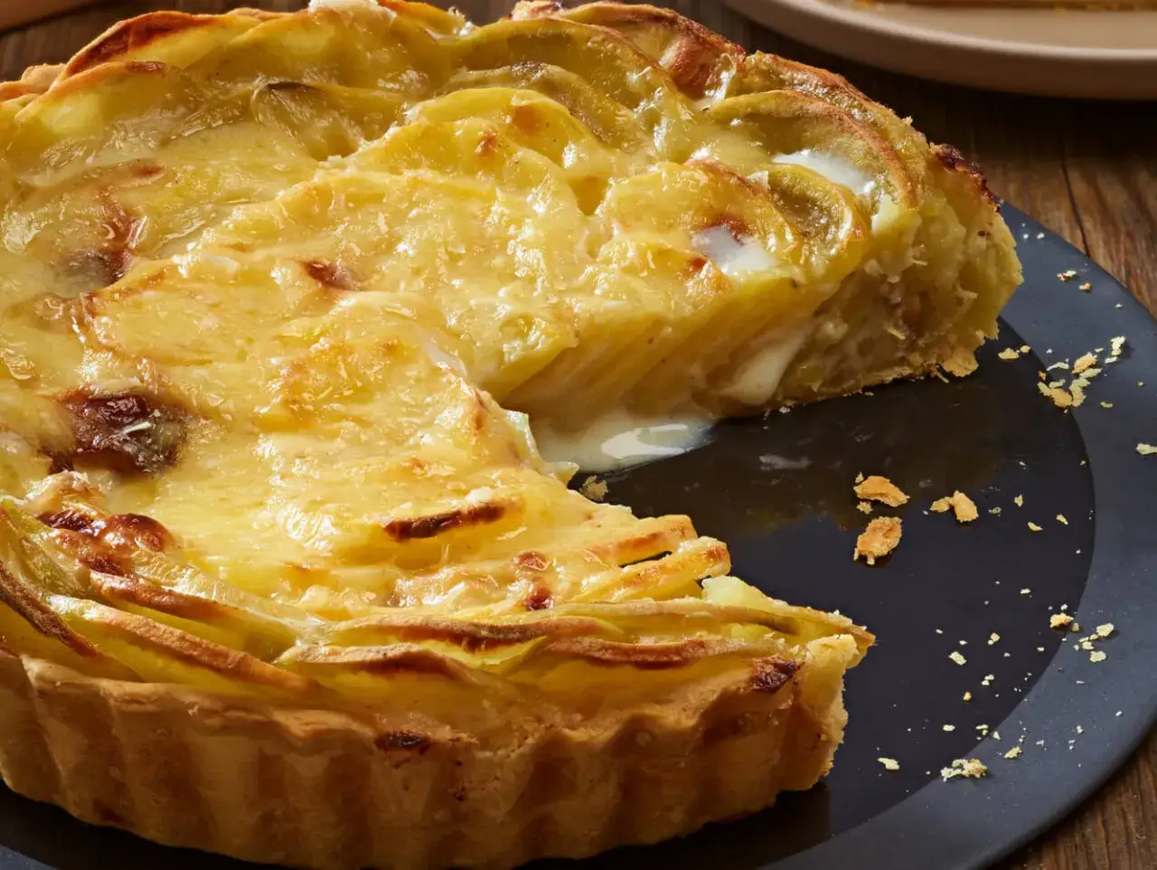 Tarte dor&eacute;e fa&ccedil;on raclette, garnie de pommes de terre fondantes et de fromage cr&eacute;meux. Une part a &eacute;t&eacute; retir&eacute;e, r&eacute;v&eacute;lant sa texture gourmande.
