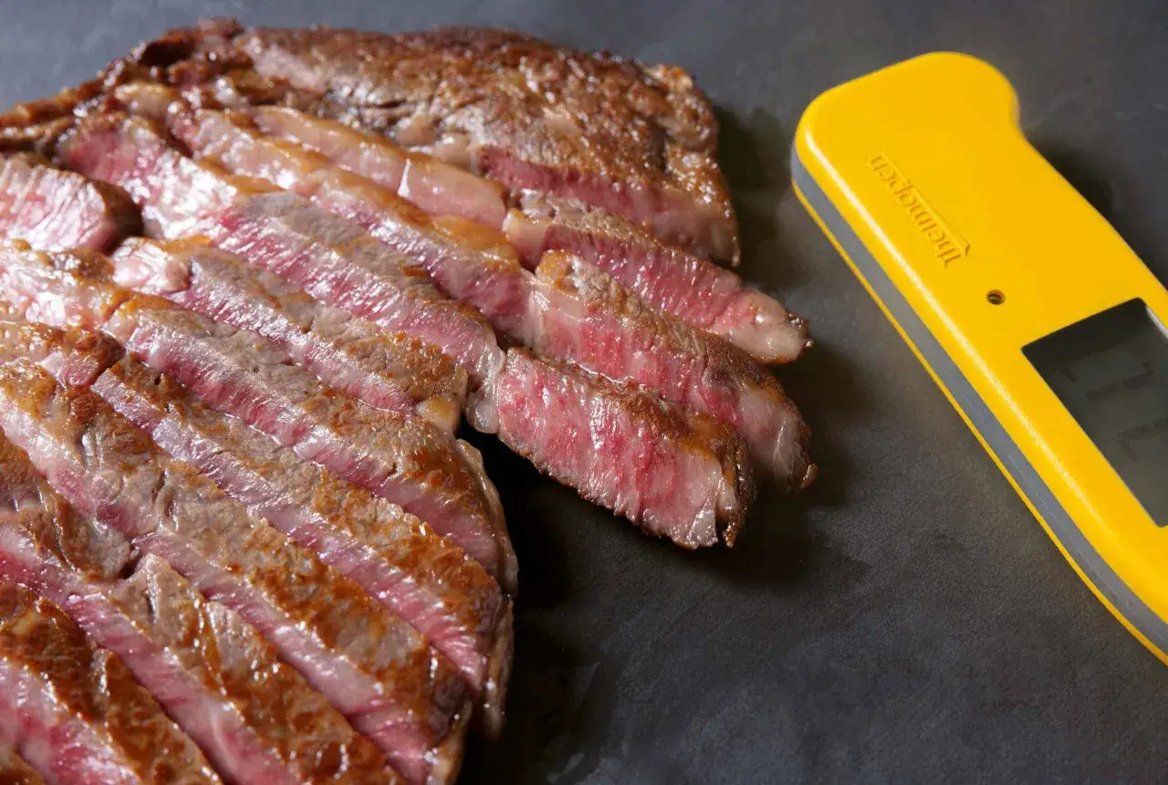 Filete de viande de kobe perfectamente cocinado, jugoso y tierno, junto a un termómetro de cocina amarillo.